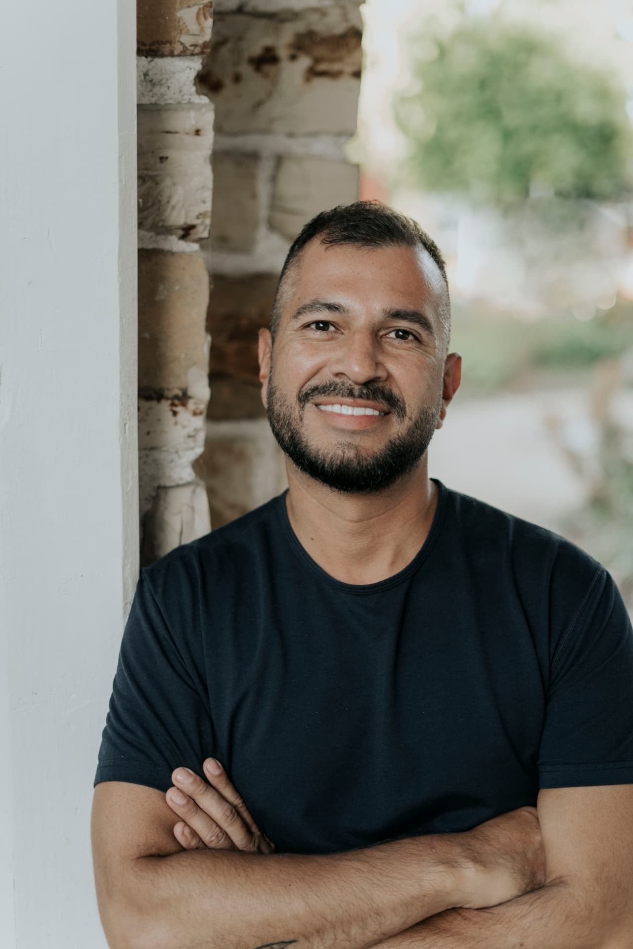 Diego Sabogal, founder of Almendra Coffee, standing with arms crossed beside a stone wall